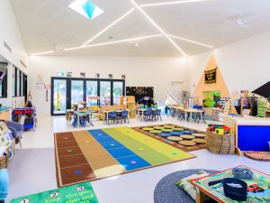 A brightly lit preschool classroom with colorful rugs, children’s tables and chairs, educational wall displays, and various play and learning stations designed for creative play and exploration.